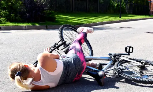 A cyclist on her side with her bicycle on a suburban road.