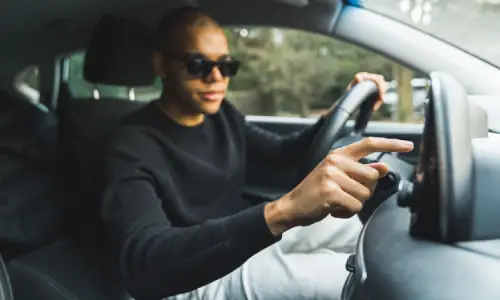 A rideshare driver wearing sunglesses adjusting the GPS device of his car.