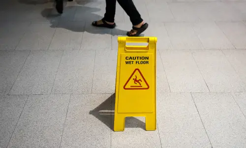 A yellow wet floor sign indoors with people walking past.