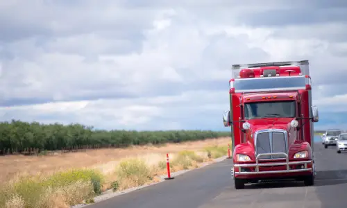 A red semi truck driving down a highway ahead of traffic on a cloudy day.