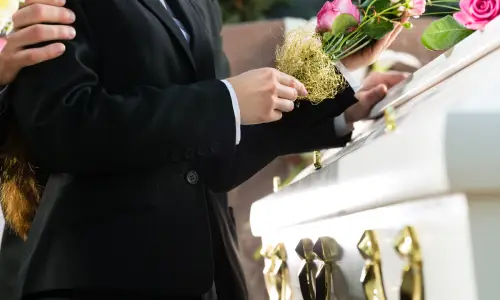 People at a funeral of a wrongful death victim leaving flowers at a white casket.