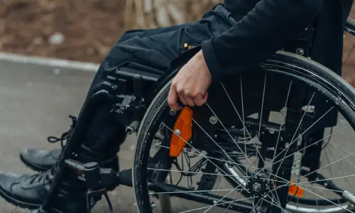 A side shot of a person in a wheelchair riding through a park.