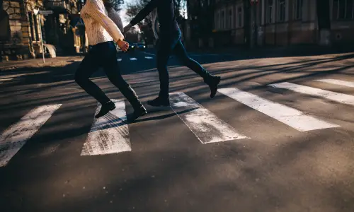 Two pedestrians running along a crossing before traffic arrives.