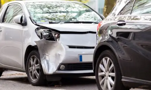 Two cars with visible damage after a collision, showing a close-up of the impact on one vehicle's front corner