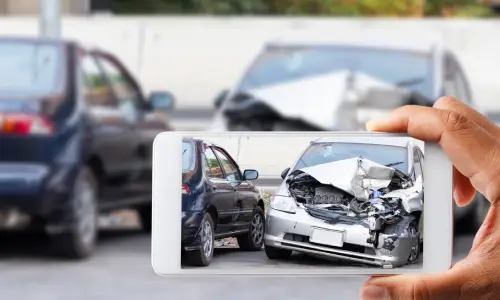 Hand holding a smartphone capturing a photo of a severe car accident, symbolizing the need for an Oakland catastrophic injury lawyer to address serious injury claims.