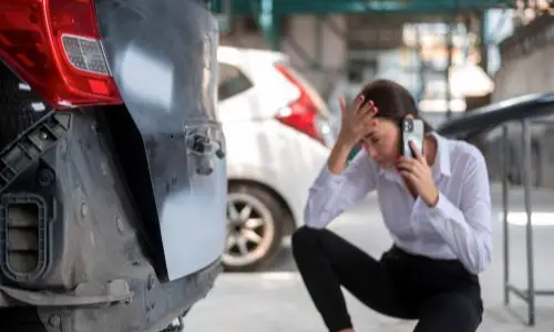 Distressed woman on the phone examining damage to a car, symbolizing the need for an Oakland Lyft accident lawyer to assist with rideshare accident claims.