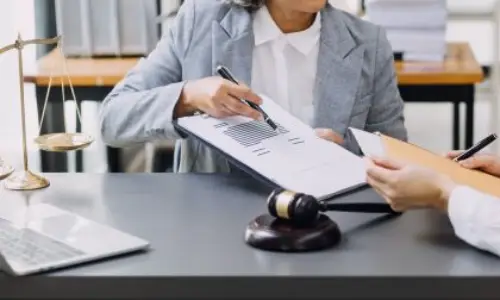 Lawyer explaining legal documents to a client in an office with a laptop, gavel, and scales of justice.